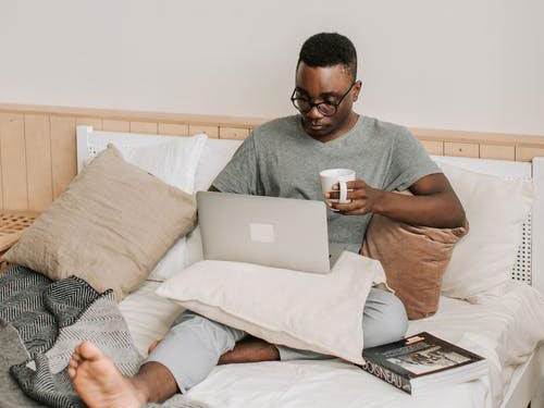 A person sitting up in bed with a laptop on their lap icon