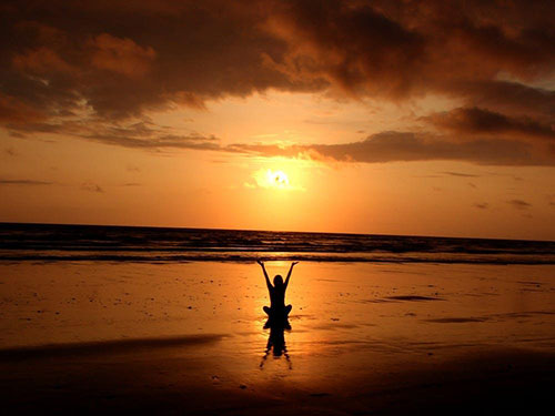 A person sitting on a beach at sunset with their arms outstretched icon