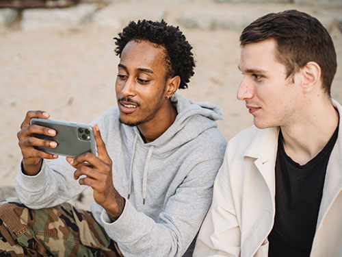 Two men sitting on a beach and looking at a phone icon