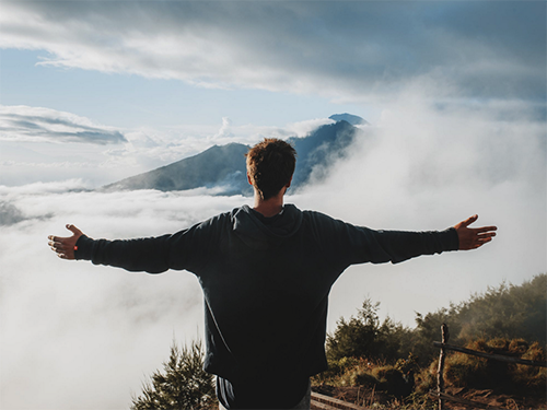 A person standing on the top of a mountain with their arms outstretched icon
