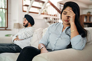 A couple sitting on the couch with one of them with her hand on her her head as if she had a headache