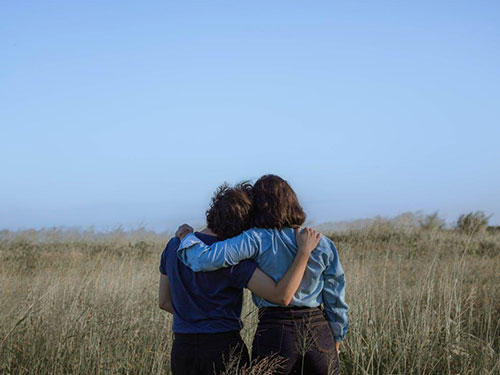 Two people in a field turned away from the camera with their arms around each other and heads on each other's shoulders icon