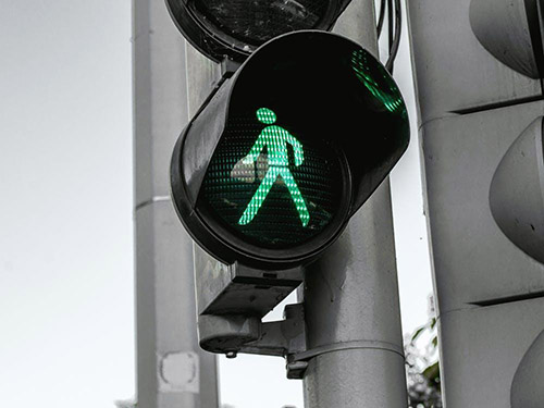 A crosswalk light with the walk figure lit up in green icon