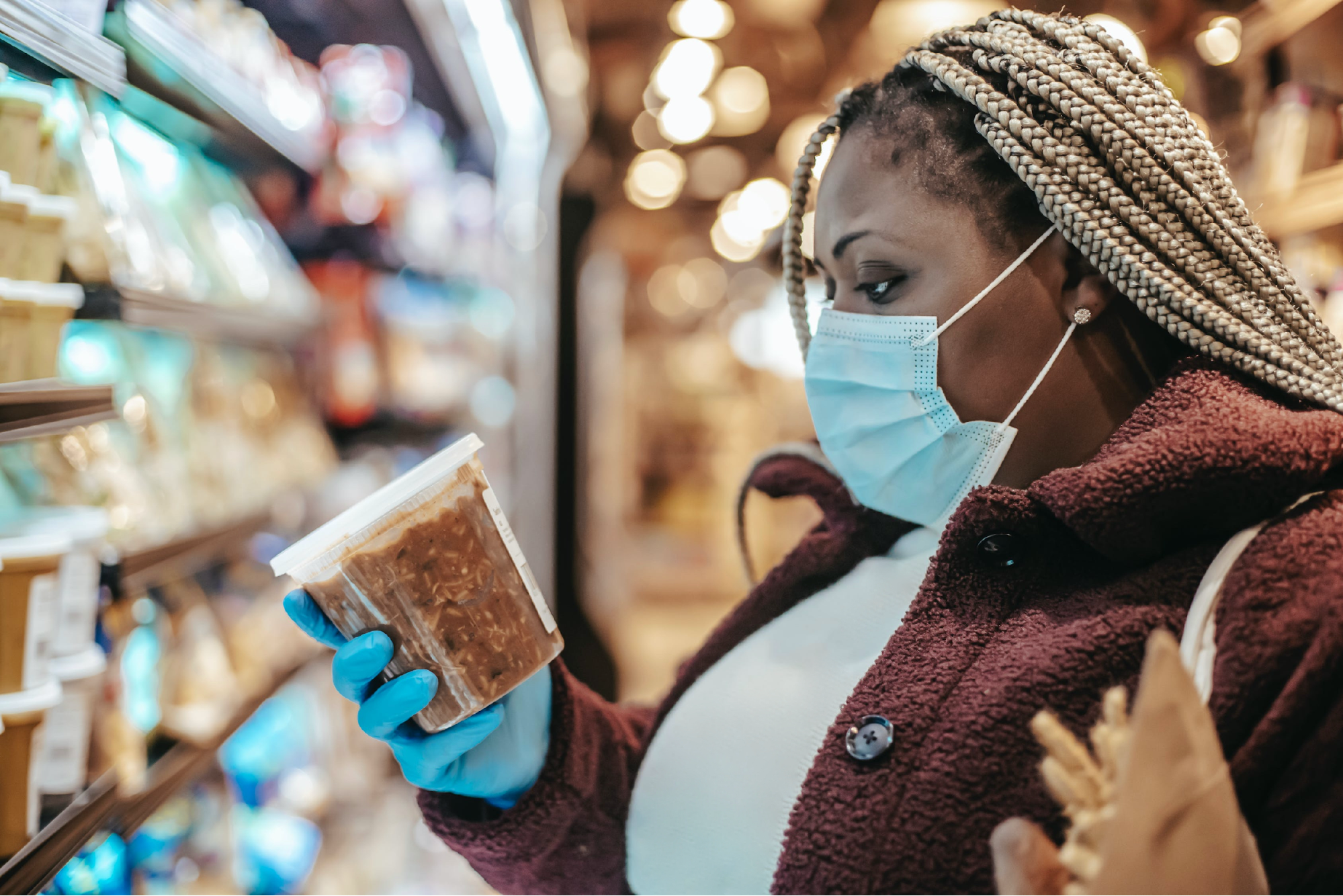 A woman wearing a mask and reading a nutrition label on a package of food in a grocery store icon