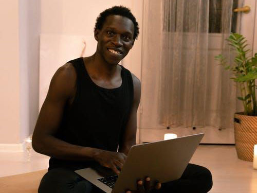 A smiling man sitting on the floor with an open laptop in his lap icon