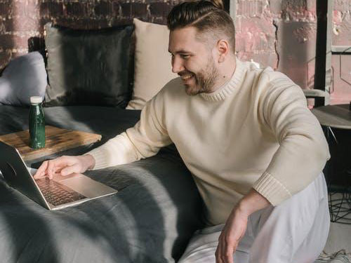 A man sitting on the floor using a laptop propped up on a bed icon