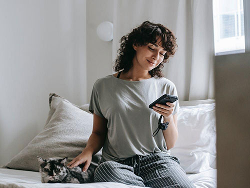 A woman sitting on a bed looking at her smartphone and smiling icon